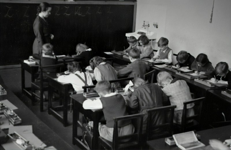 Alunos escrevendo cartas em sala de aula durante atividade de primeiro dia de aula com cápsula do tempo