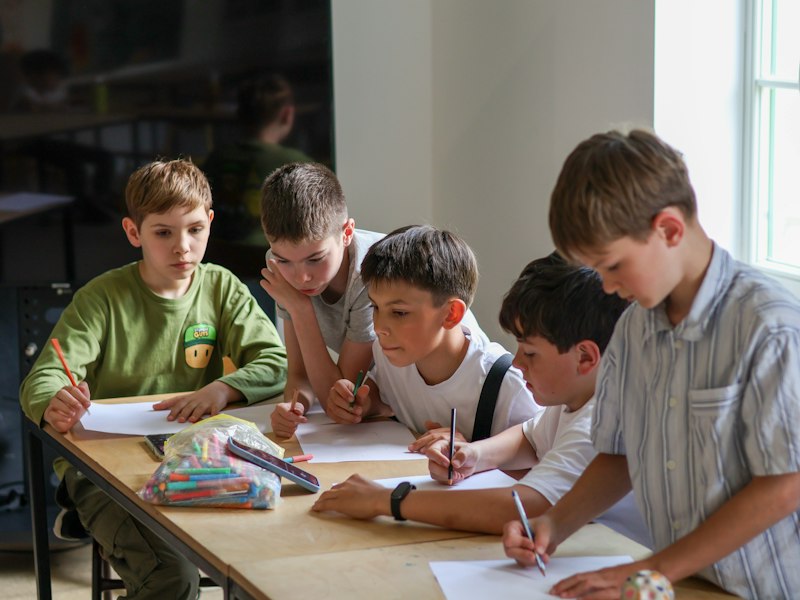 Alunos escrevendo cartas para o futuro em sala de aula durante atividade de cápsula do tempo