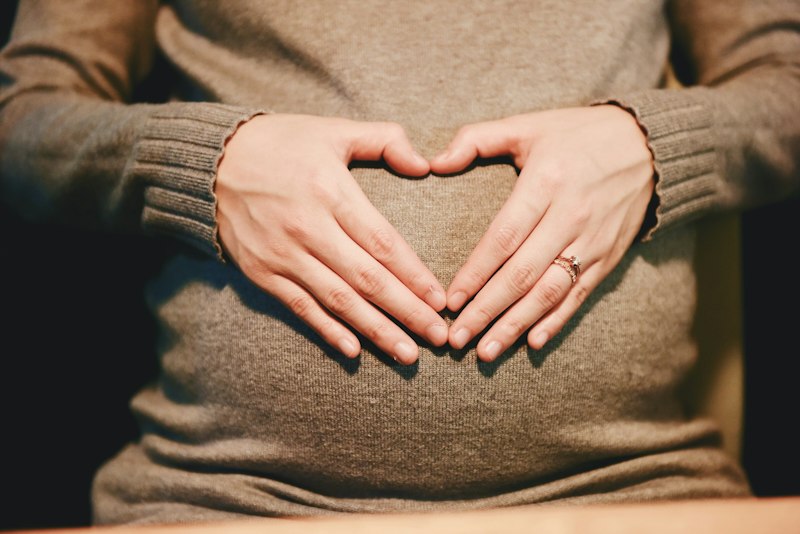 Mãos formando um coração sobre a barriga de gestante, simbolizando uma mensagem para o bebê que vai nascer