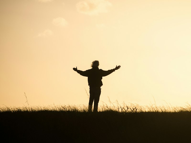 Pessoa em momento de reflexão e gratidão ao pôr do sol, representando o exercício de olhar para a própria vida com apreciação
